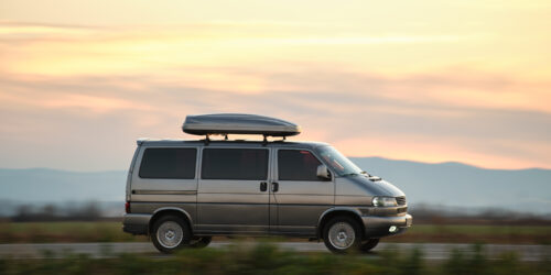 Passenger van with roof rack driving fast on intercity road at sunset. Highway traffic in evening