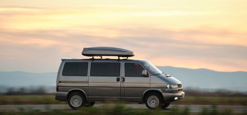 Passenger van with roof rack driving fast on intercity road at sunset. Highway traffic in evening