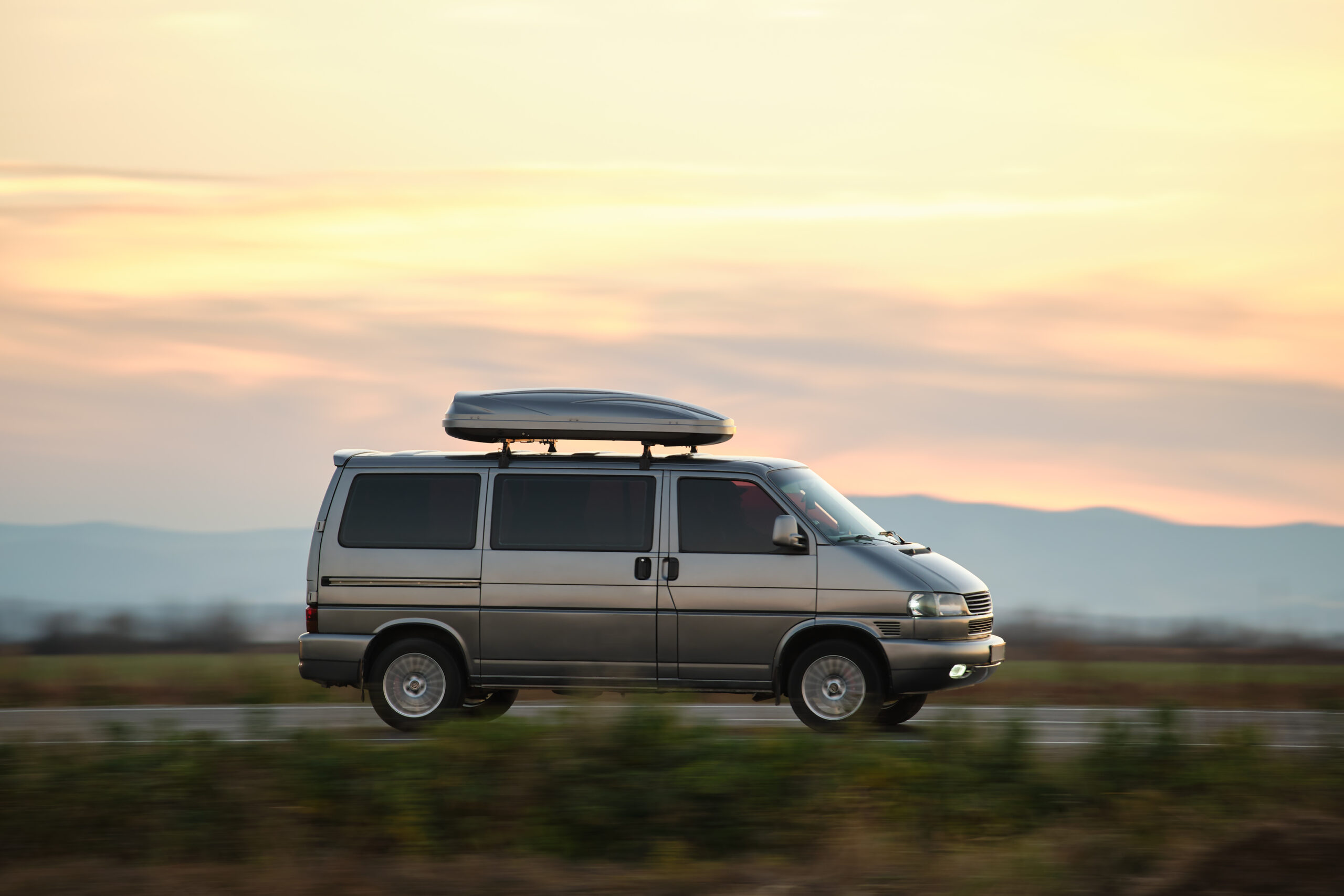 Passenger van with roof rack driving fast on intercity road at sunset. Highway traffic in evening